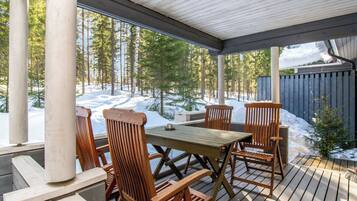 En träveranda med ett bord och stolar, med utsikt över ett snötäckt landskap med träd.