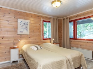 A wooden-paneled room with a bed, bedside table, lamp, and a window with curtains. - Vacation home Reppu by Interhome (Sotkamo)
