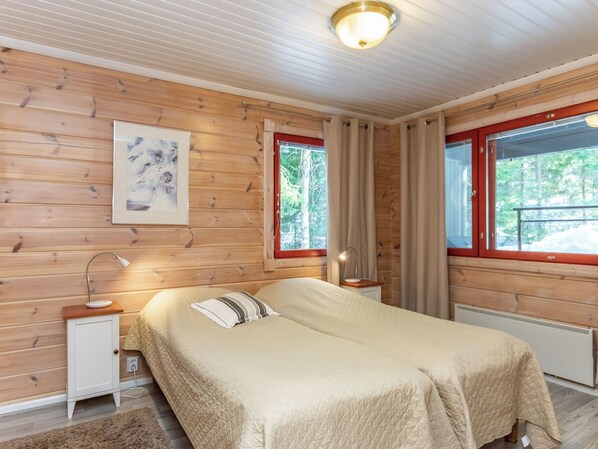 A wooden-paneled room with a bed, bedside table, lamp, and a window with curtains.