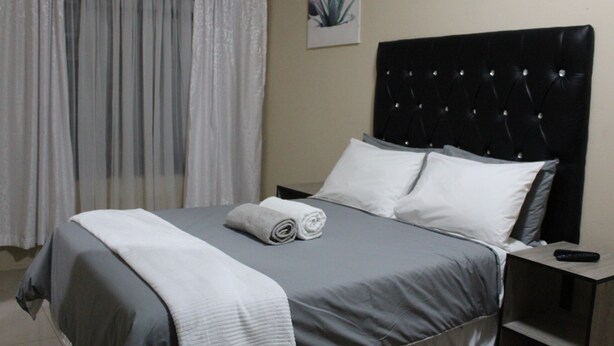 A neatly made bed with a grey and white duvet, a rolled white towel, and a black headboard. - M n M Guest House in Polokwane Turfloop (Polokwane)