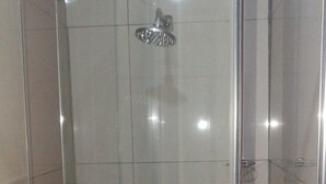 A glass-enclosed shower stall with a handheld showerhead, tiled walls, and a visible drain. - M n M Guest House in Polokwane Turfloop (Polokwane)