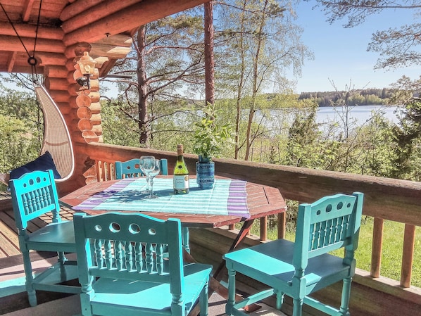 Terraza de madera con mesa y sillas, con vista a un lago.