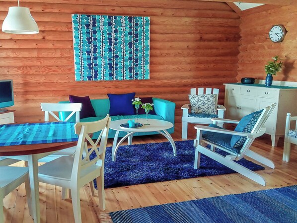 A cozy living room with a wooden interior, a blue sofa, a small round table, and a white chair. - Kesärinne by Interhome (Ikaalinen)