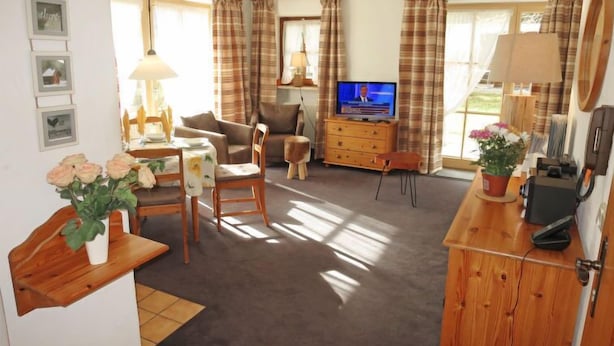 Ett vardagsrum med en soffa, ett tv-appar, ett träskåp och en matplats med ett bord och stolar.