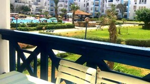 Un balcon donnant sur une piscine, des palmiers et un ensemble de bâtiments en arrière-plan.