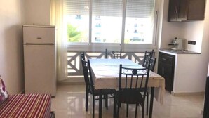 A compact kitchen with a dining table and chairs, a refrigerator, and a window with blinds. - Residence Cite Jardin 4089 (Martil)