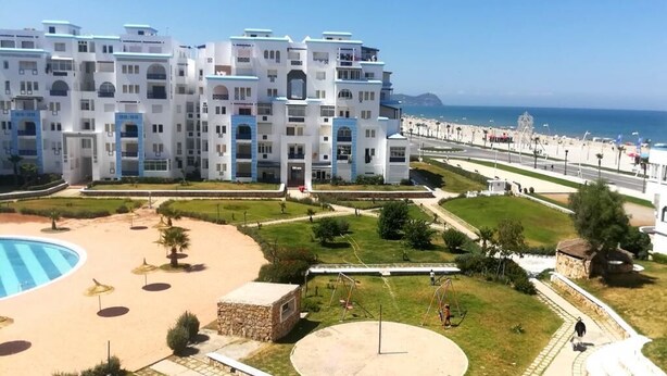 A modern hotel with multiple floors, a pool, and a beach view. - Residence Cite Jardin 4089 (Martil)