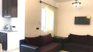 A living room with two dark sofas, a flat-screen TV, a ceiling light fixture, and a window with curtains. - Residence Cite Jardin 4089 (Martil)