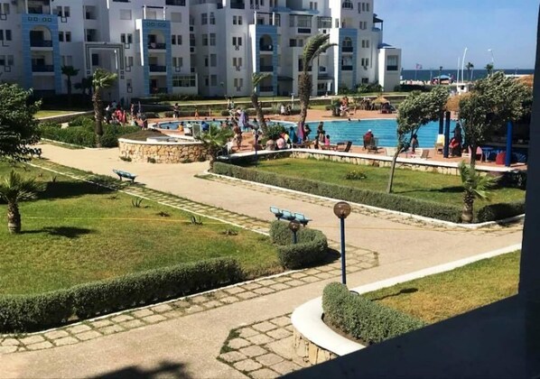 A hotel courtyard with a swimming pool, palm trees, and a well-maintained lawn.