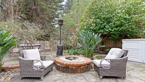 A patio with wicker furniture, a stone fire pit, and a lantern. - Pot Belly Beach House (Aptos)
