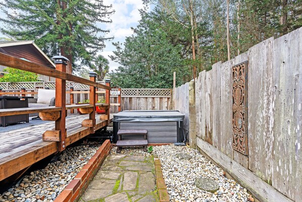 Una terraza de madera con un jacuzzi, un sendero de piedra y una valla de madera con detalles de metal decorativo.