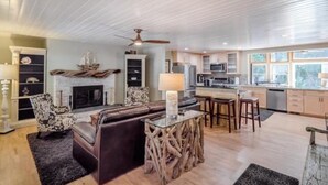 A spacious living area with a fireplace, a dining area with stools, and a kitchen with modern appliances. - Pot Belly Beach House (Aptos)