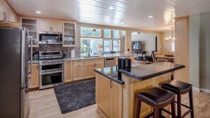 A modern kitchen with wooden cabinets, stainless steel appliances, and a large island with bar stools. - Pot Belly Beach House (Aptos)