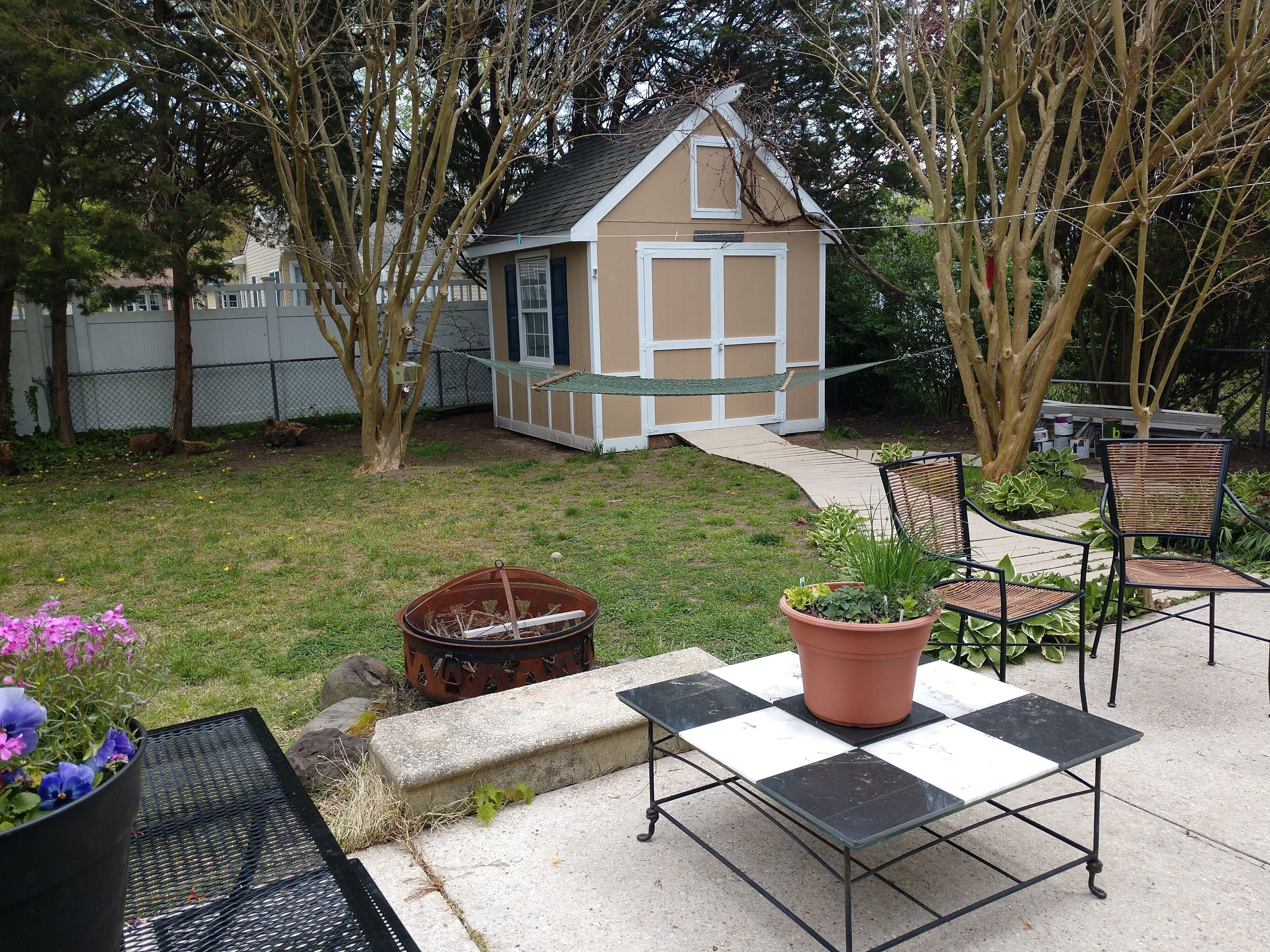 A backyard with a small shed, a patio table, chairs, and potted plants.