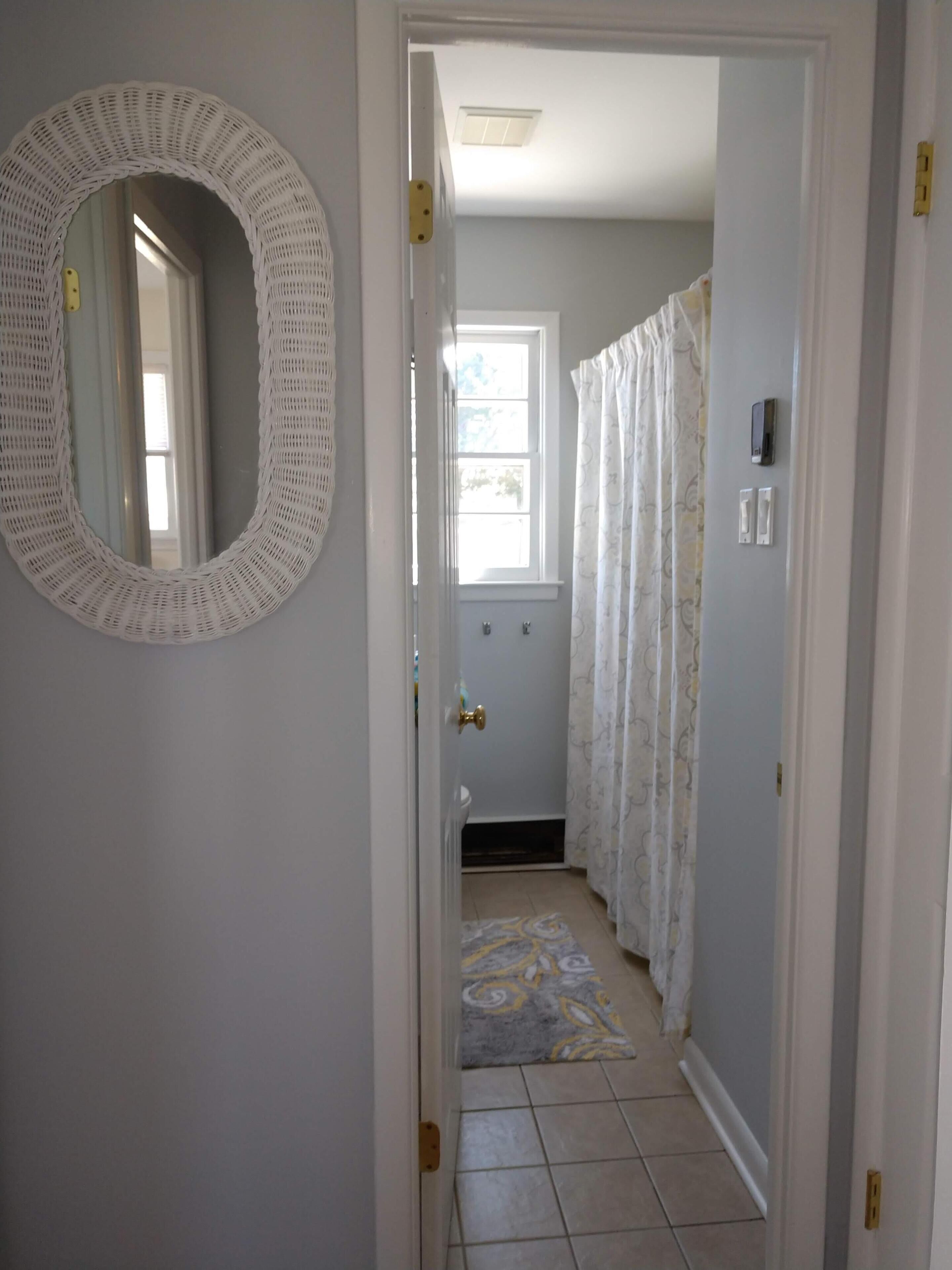 A hallway with a white door, a mirror, a patterned rug, and a shower with a curtain.