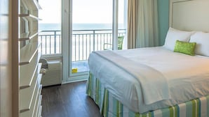 Una habitación de hotel con cama, ventana con vista al mar, una silla y un aparador.