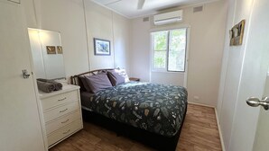 Une chambre à coucher comprenant un lit, une commode, une fenêtre et un appareil de climatisation.