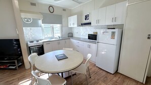 Une cuisine compacte avec des meubles blancs, un four à micro-ondes, un réfrigérateur et une table à manger avec des chaises.