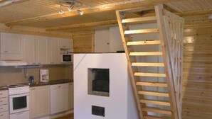 Una cocina compacta con armarios blancos, un microondas y un horno empotrado. Una escalera de madera está apoyada en la pared, y se ve una ventana pequeña.