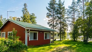 A red wooden cabin with a green roof, surrounded by lush greenery and tall trees. - Saniainen 5 by Interhome (Pielavesi)