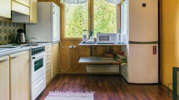 A compact kitchen with wooden cabinets, a stove, a microwave, and a refrigerator.