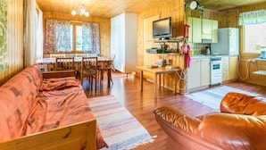 A cozy cabin interior with a wooden dining area, a sofa, a leather armchair, and a kitchen with basic appliances. - Saniainen 5 by Interhome (Pielavesi)