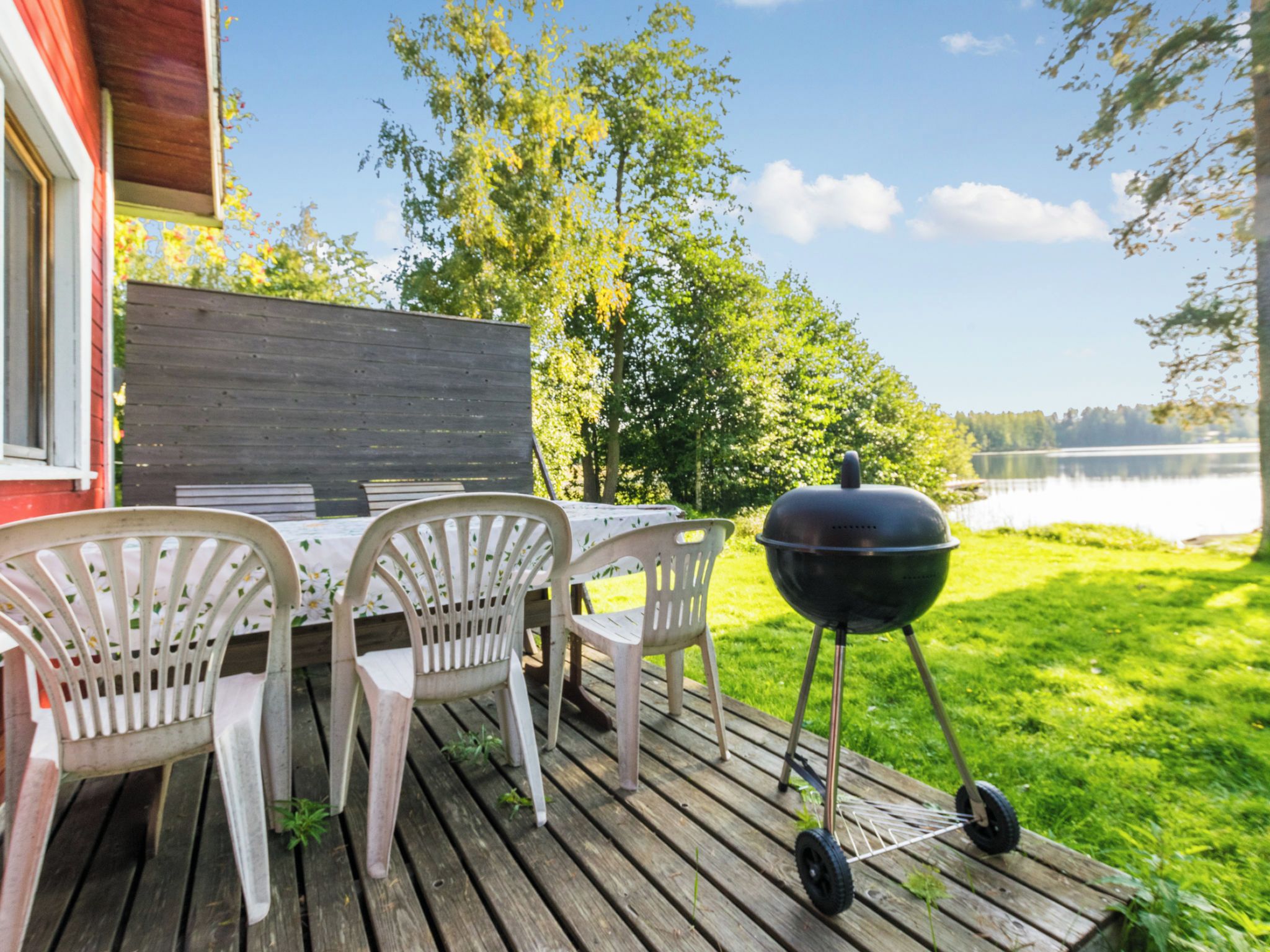 Una terraza de madera con una mesa, sillas, una parrilla y vistas a un lago.