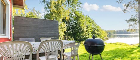A wooden deck with a table and chairs, a barbecue grill, and a view of a lake.