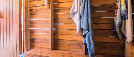 A wooden bench with towels hanging on a rack, a wooden wall, and a small trash bin.