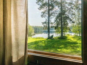 Una ventana con vistas a un lago, árboles y césped.