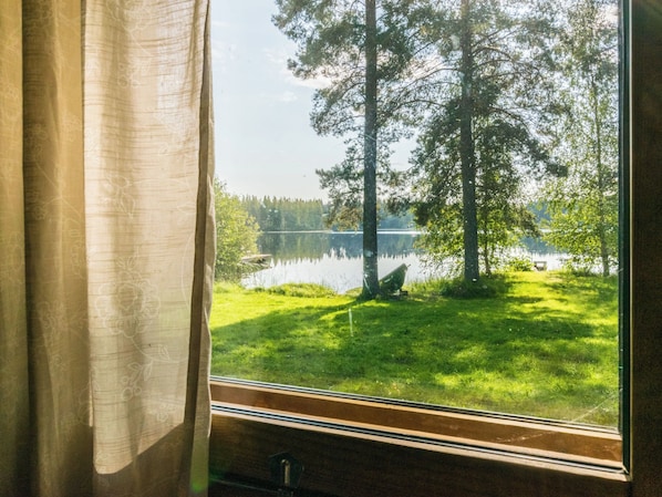 A window with a view of a lake, trees, and grass.
