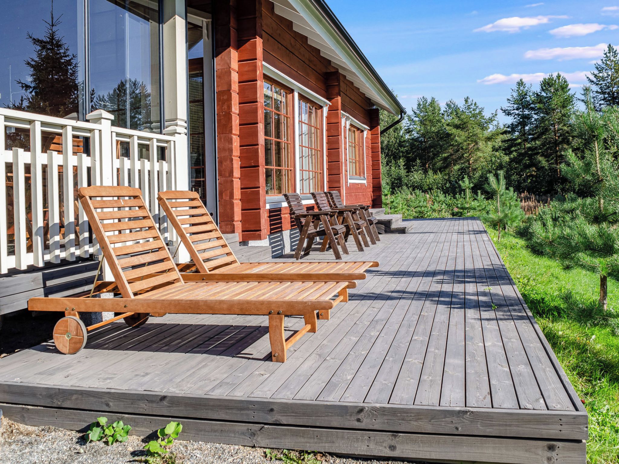 Eine Holzterrasse mit Liegestühlen und ein Gebäude mit großen Fenstern und einem weißen Geländer.