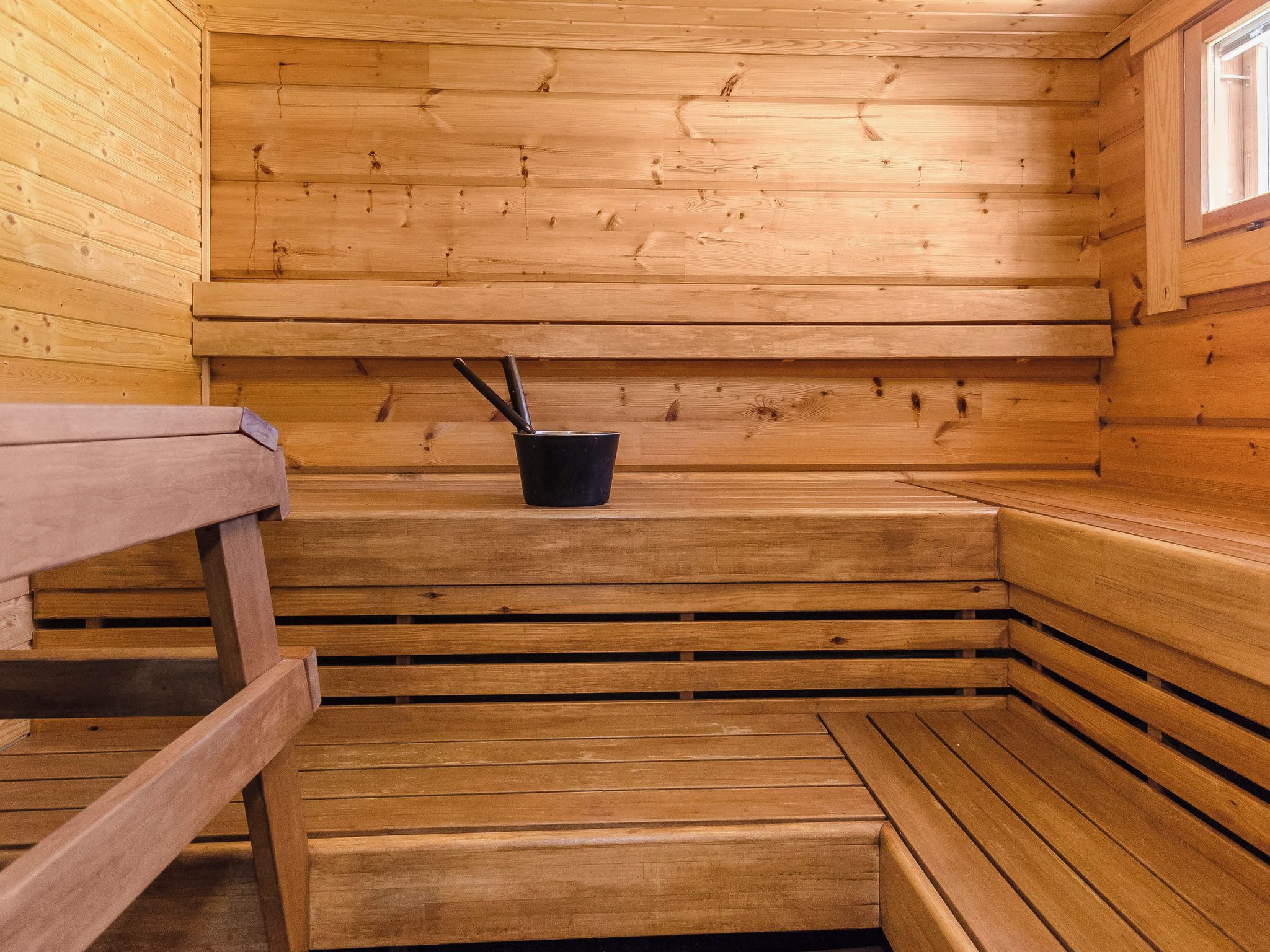 Ein Saunaraum mit Holzsitzen und einem schwarzen Eimer mit Wasserschöpfer.
