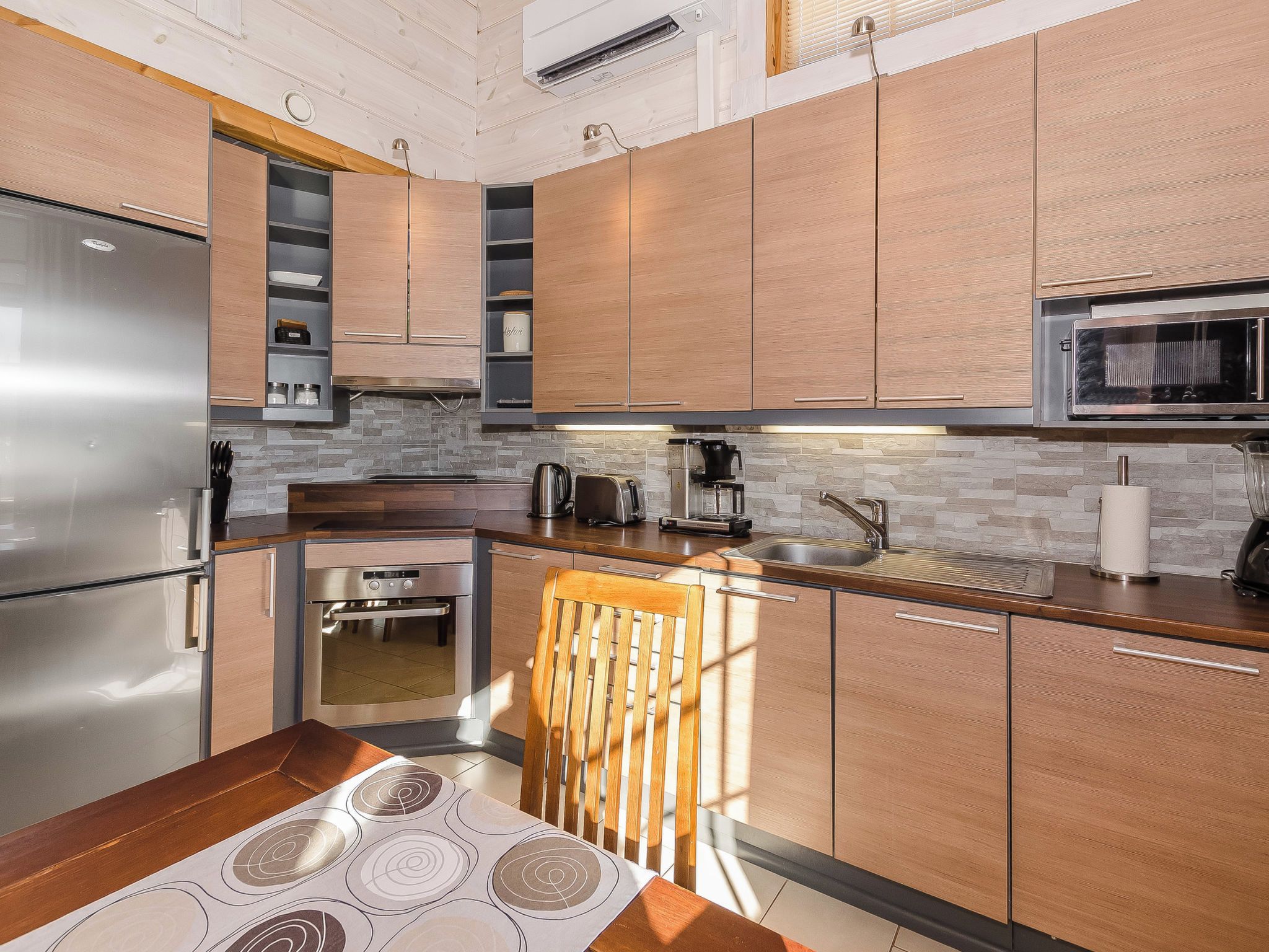 A modern kitchen with stainless steel appliances, wooden cabinets, and a stone backsplash.