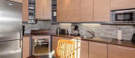 A modern kitchen with stainless steel appliances, wooden cabinets, and a stone backsplash.