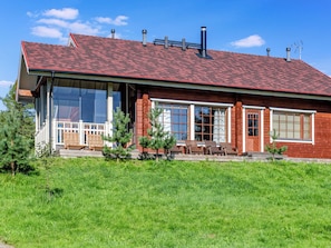 Ein zweistöckiges Haus mit rotem Ziegeldach, großen Fenstern und einer Veranda mit Gartenmöbeln.