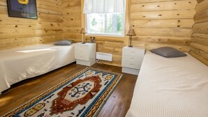 Une chambre dans un chalet en bois, avec deux lits, une fenêtre avec des rideaux, un radiateur et un tapis.