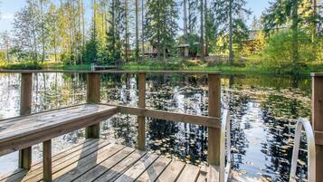 A wooden dock extending over a calm lake with reflections of trees and a cabin in the background.