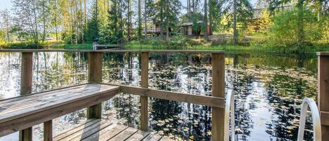 A wooden dock extending over a calm lake with reflections of trees and a cabin in the background.