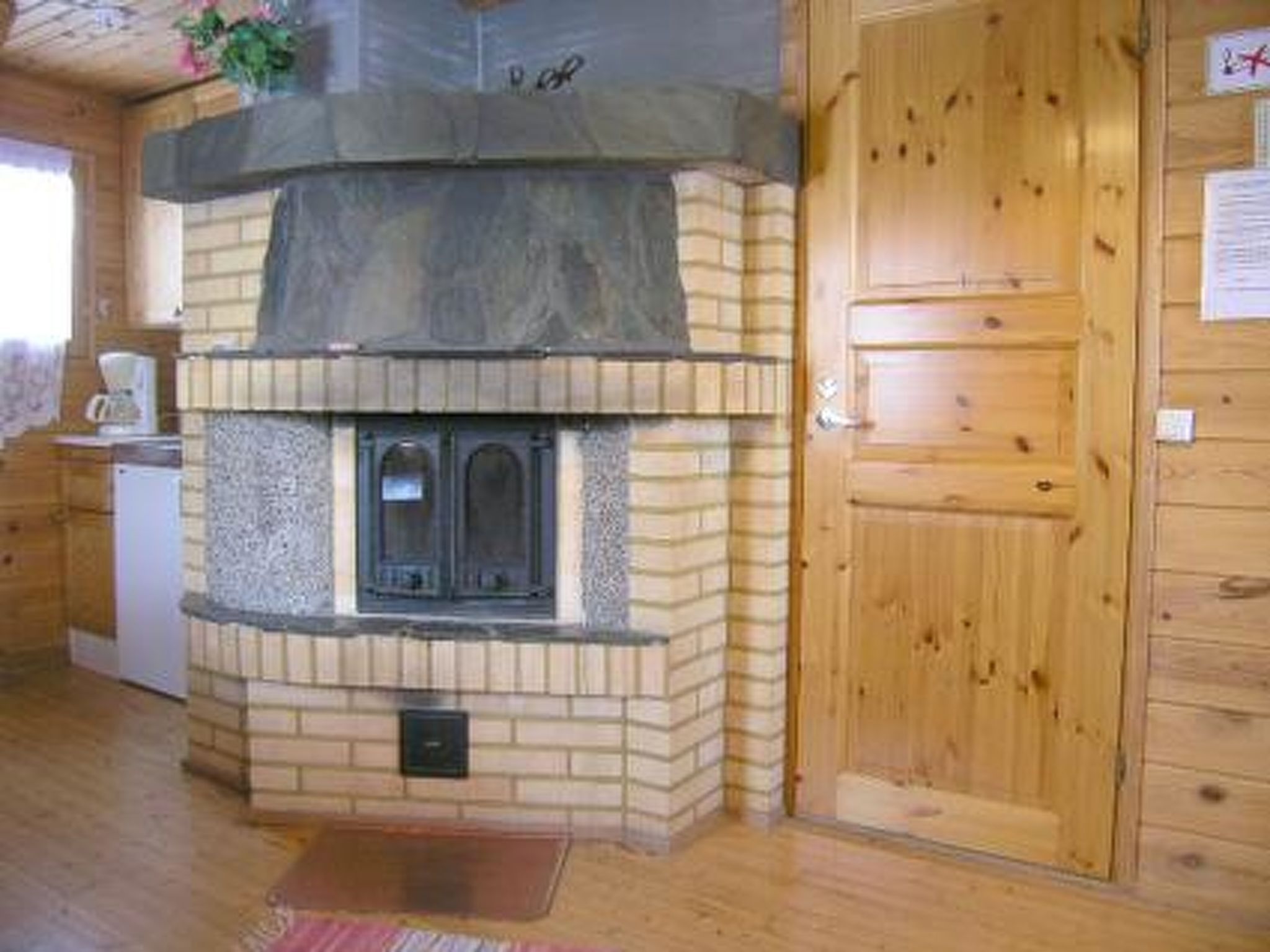 A wooden interior with a stone fireplace, a wooden door, and a small white appliance.