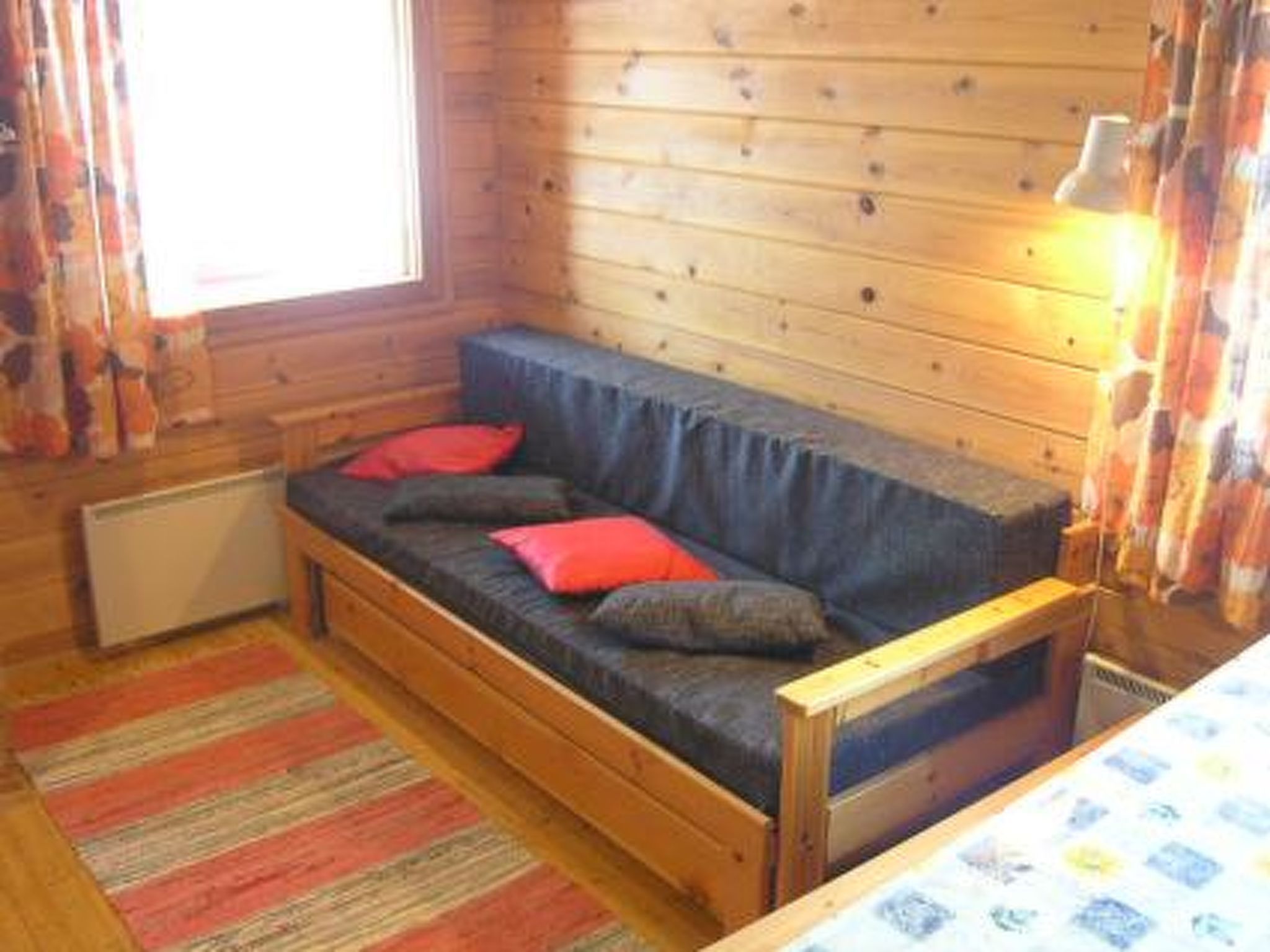 Een gezellig cabin interieur met een banksofa van hout, een radiator en een gestreept vloerkleed.