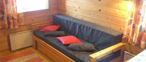 L’intérieur chaleureux d’un chalet avec un canapé-banquette en bois, un radiateur et un tapis à rayures.