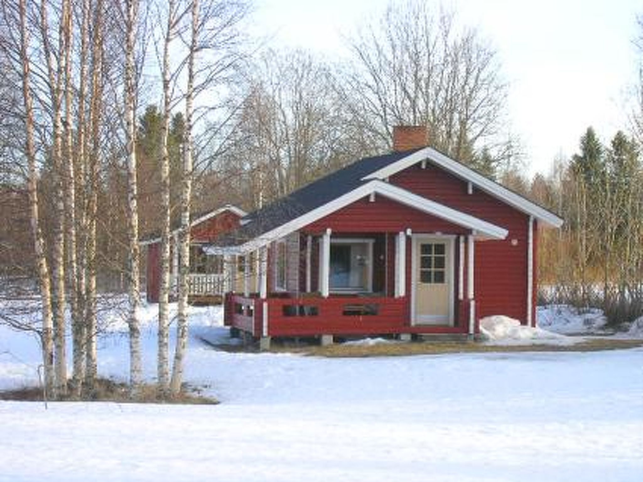 A small red cabin with a porch, surrounded by snow and trees.