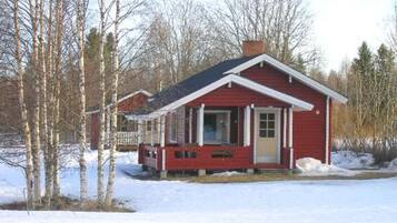 A small red cabin with a porch, surrounded by snow and trees.