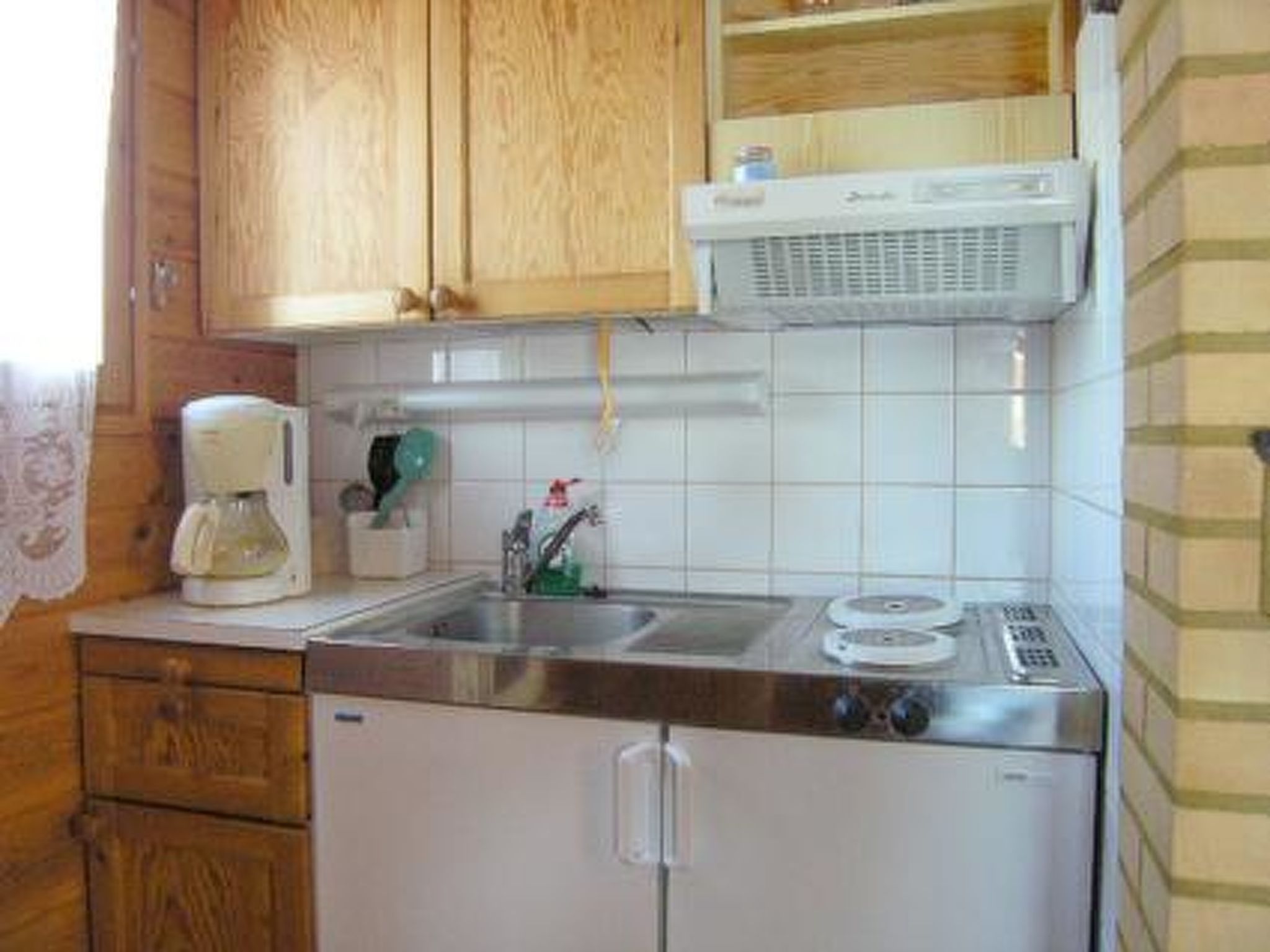 Een compacte keuken met houten kastjes, een ingebouwde magnetron, een koffiezetapparaat en een klein spoelgedeelte.