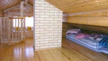 A wooden cabin interior with a bunk bed, a wooden floor, and a brick wall.
