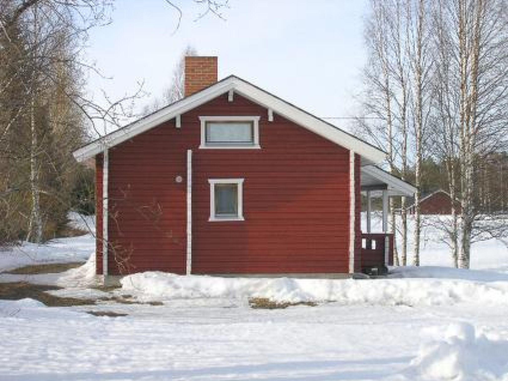 Une maison en bois rouge, avec un toit à pignon, une cheminée et un petit porche.