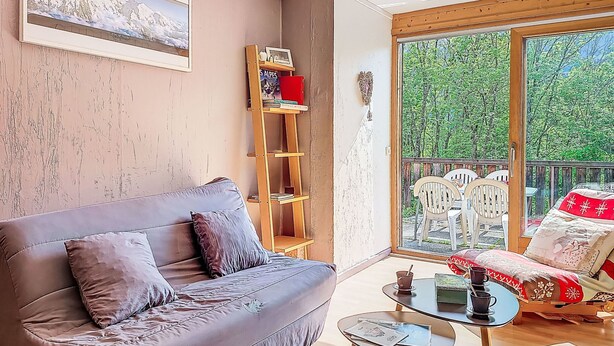 Ein Wohnzimmer mit einer Couch, einem kleinen Tisch, einem Bücherregal und einem Balkon mit Gartenmöbeln.