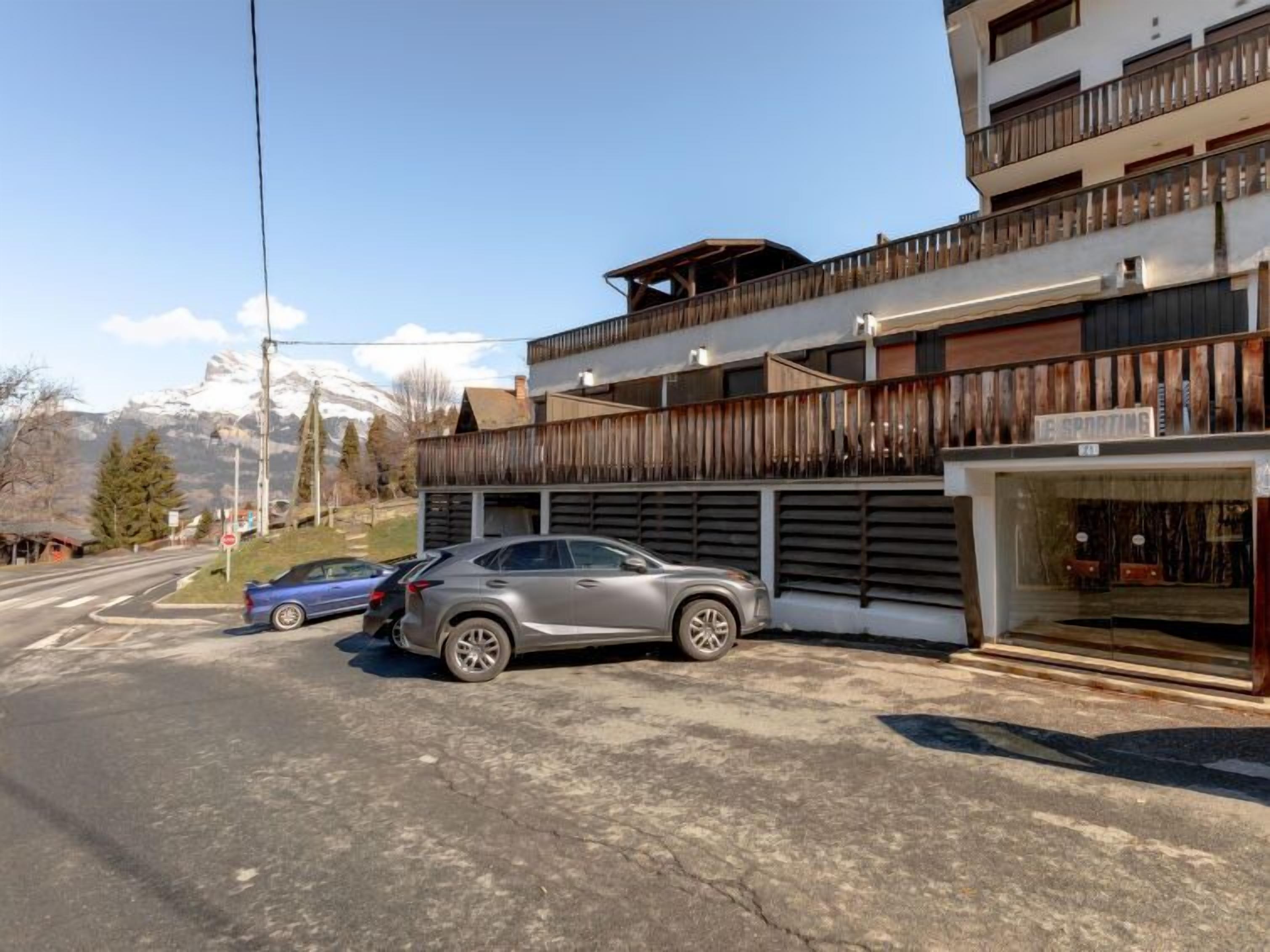 A modern building with a wooden balcony, a shop on the ground floor, and a mountain view in the background.