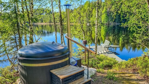 A sauna with a large black dome, wooden steps, and a wooden deck overlooking a lake.